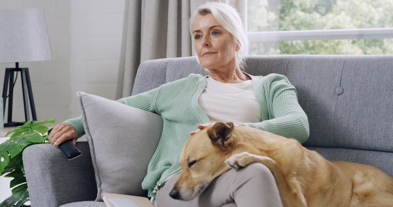 Kvinna sitter i en soffa med en hunds huvud vilande i knät.