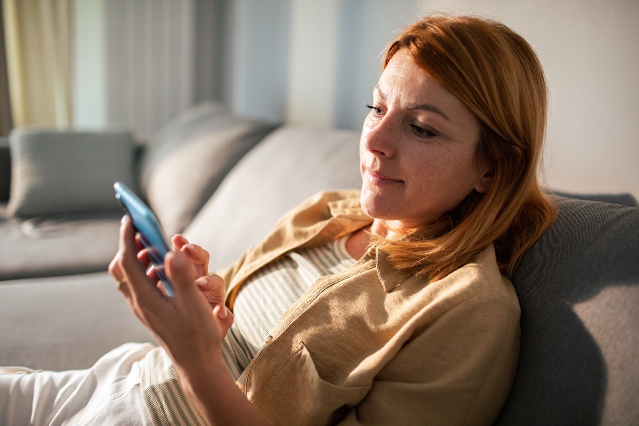Kvinna sitter i soffa och tittar på sin mobiltelefon.