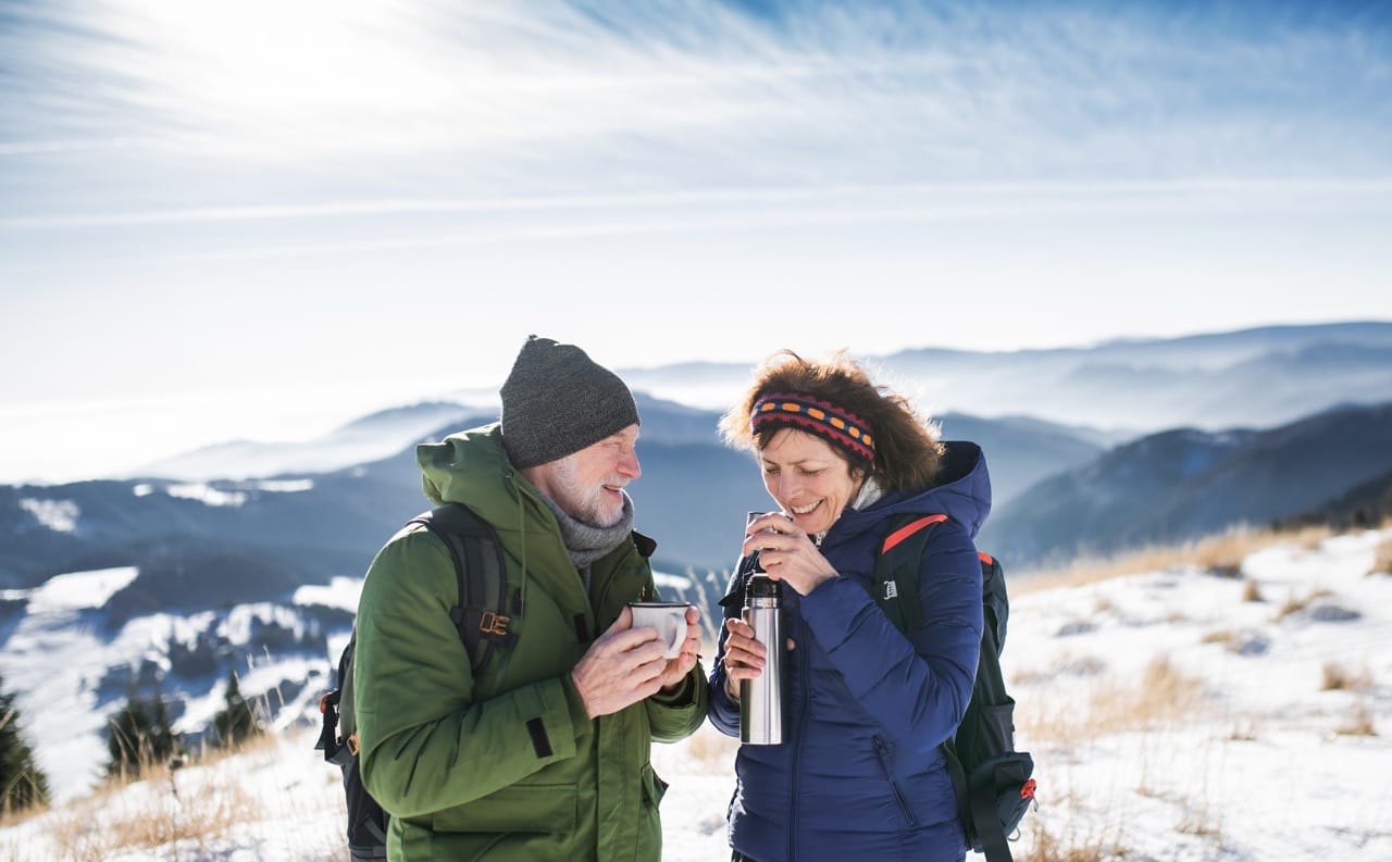Man och kvinna dricker kaffe ståendes i snö på ett fjäll.