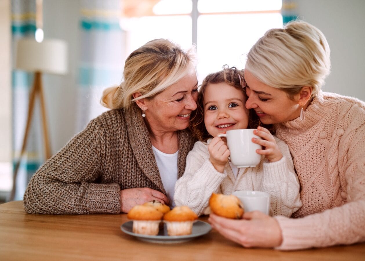 Tre generationer, mor, dotter och barnbarn fikar vid bord.
